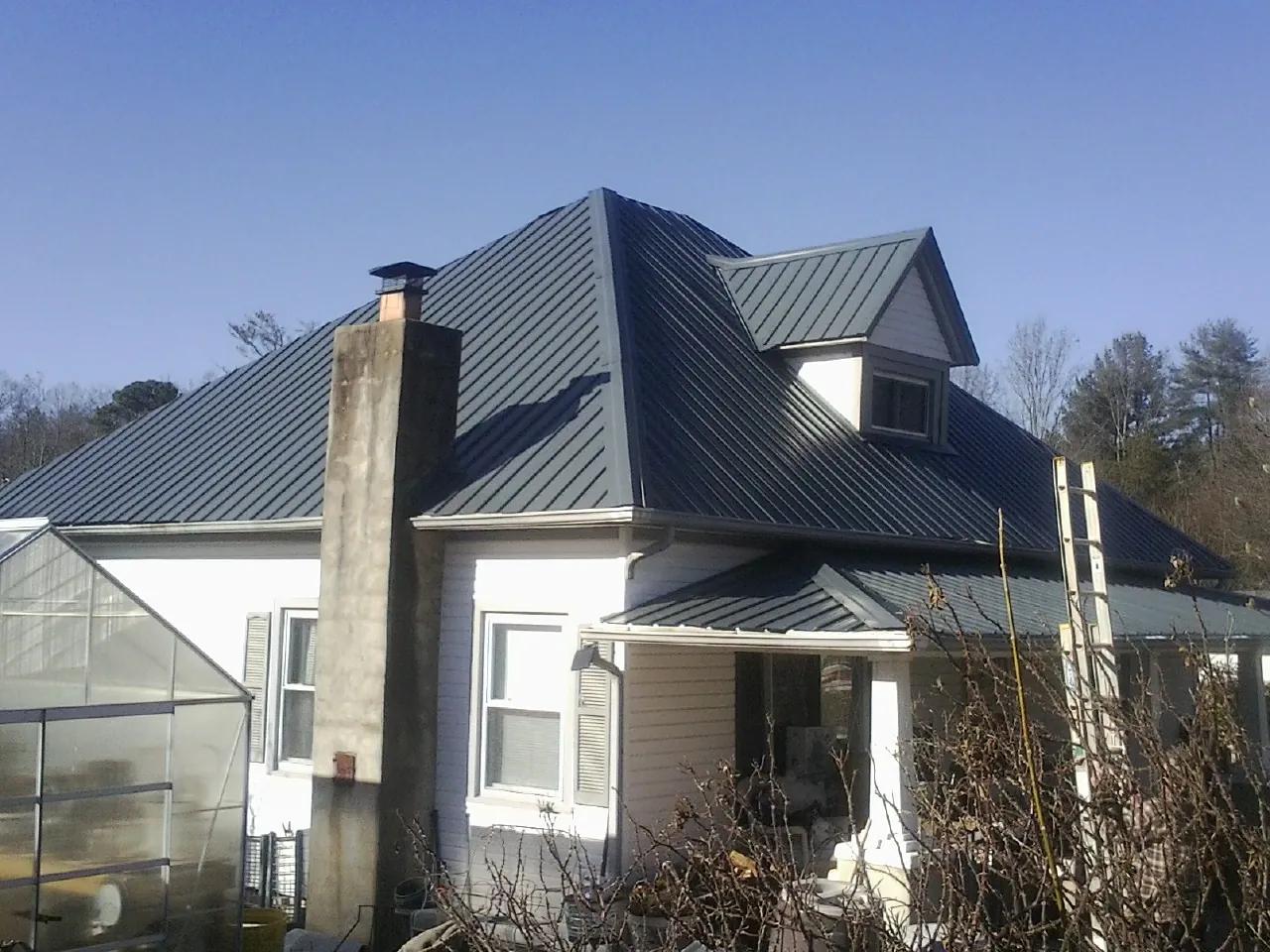 Dark blue standing seam metal roof on a white farmhouse with dormer — Slate & Tile Roof Repair by Roofing Brothers in Tunnelton