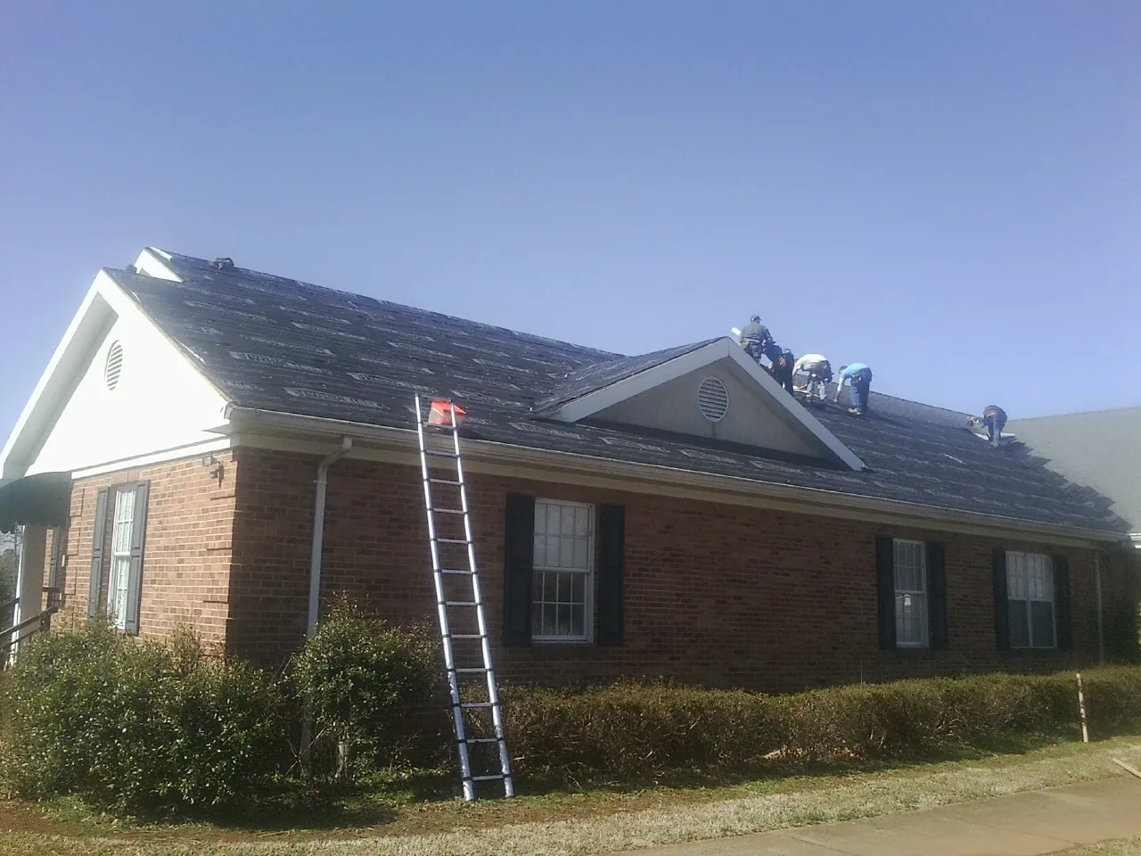 Crew tearing shingles off a brick ranch roof with a ladder set — Metal Roof Repair work by our crew in Tunnelton