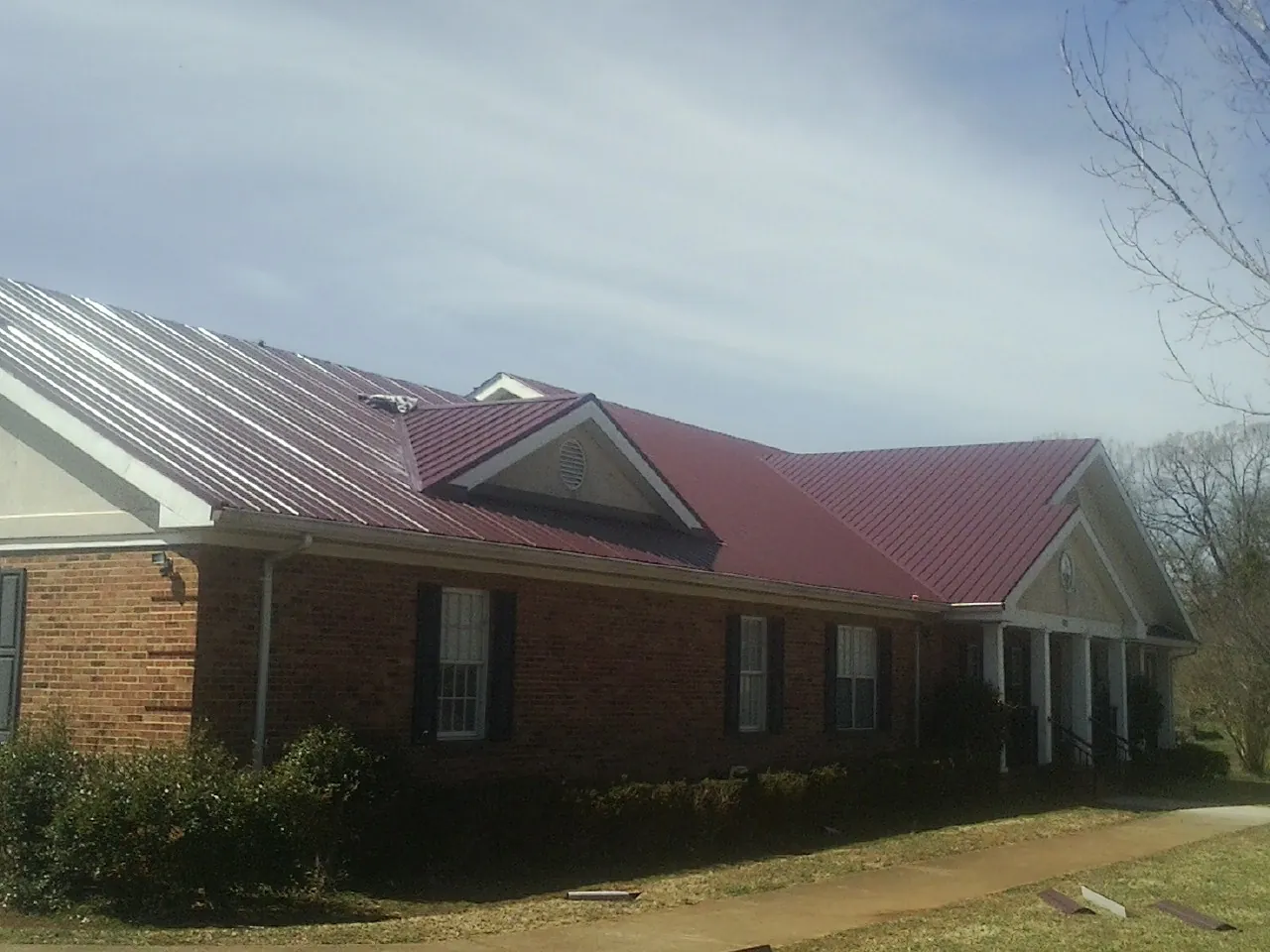 Red metal roof with gabled entries on a long brick building, from a Hail Damage Roof Repair job in Tunnelton