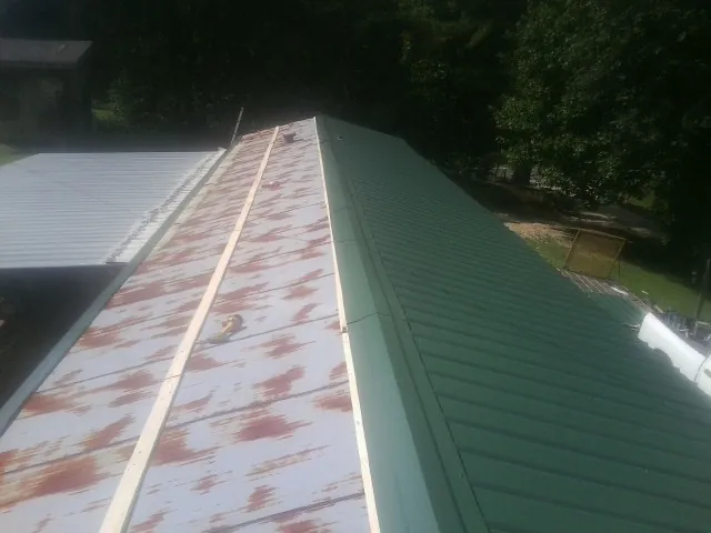 Old rusted panels beside newly installed green metal roofing — Wind Damage Roof Repair by Roofing Brothers in Tunnelton