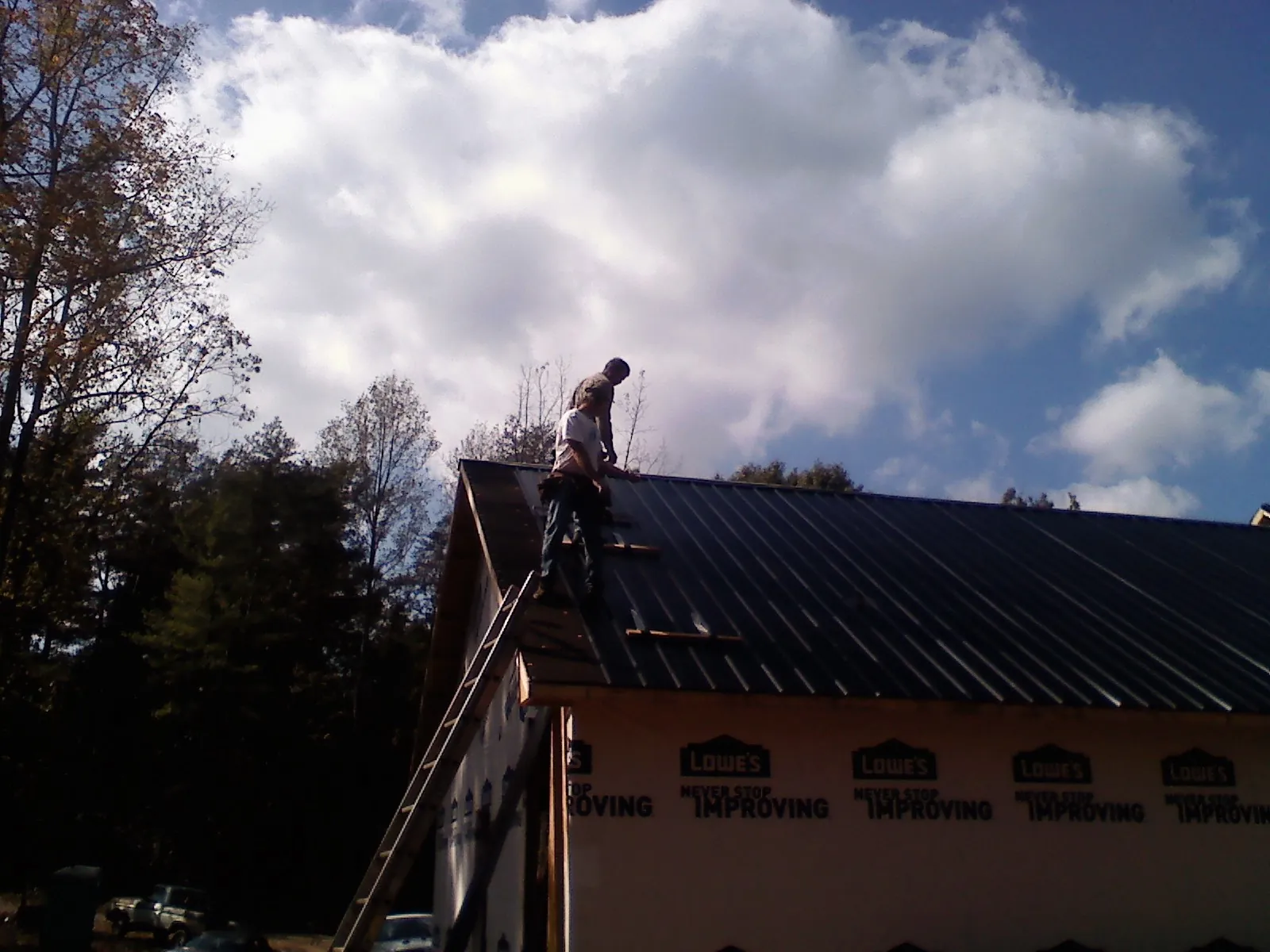 Roofer fastening dark metal panels high against a cloudy sky, from a Roof Inspection job in Tunnelton