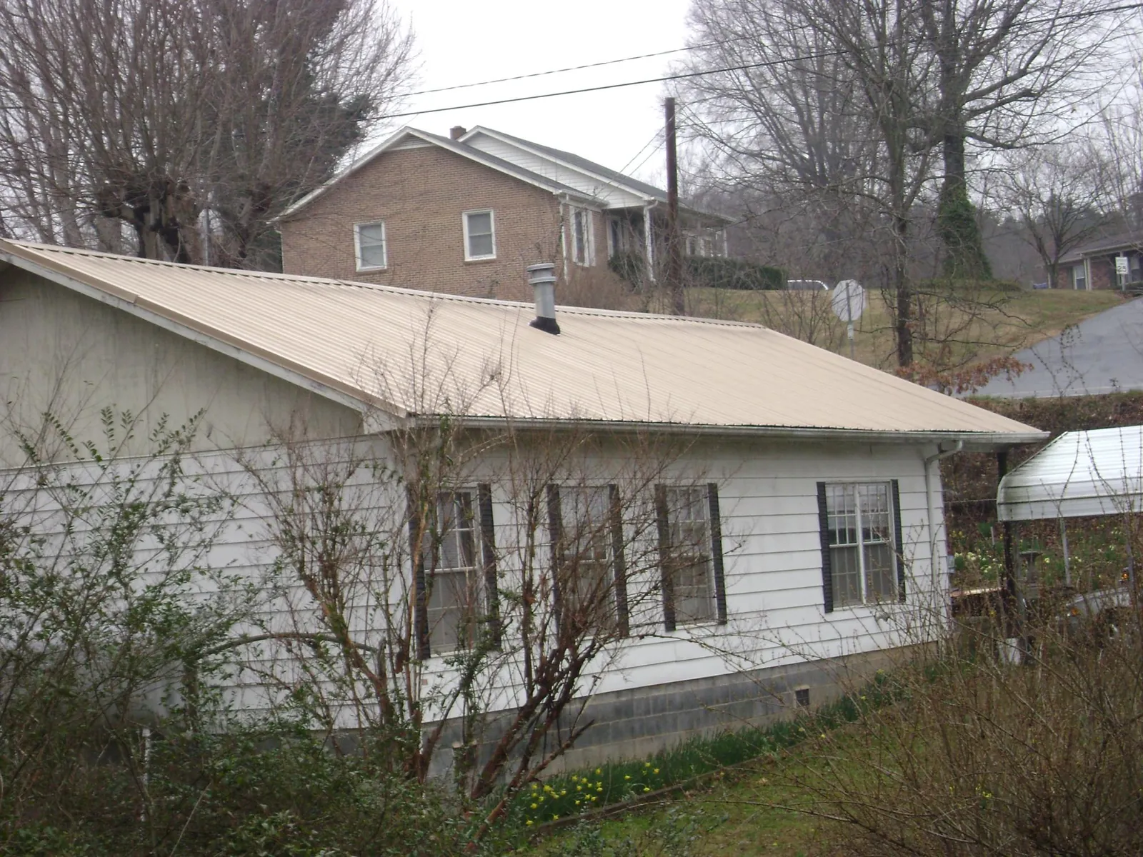 Tan metal roof on a white sided house set into a hillside — Commercial Roofing by Roofing Brothers in Tunnelton